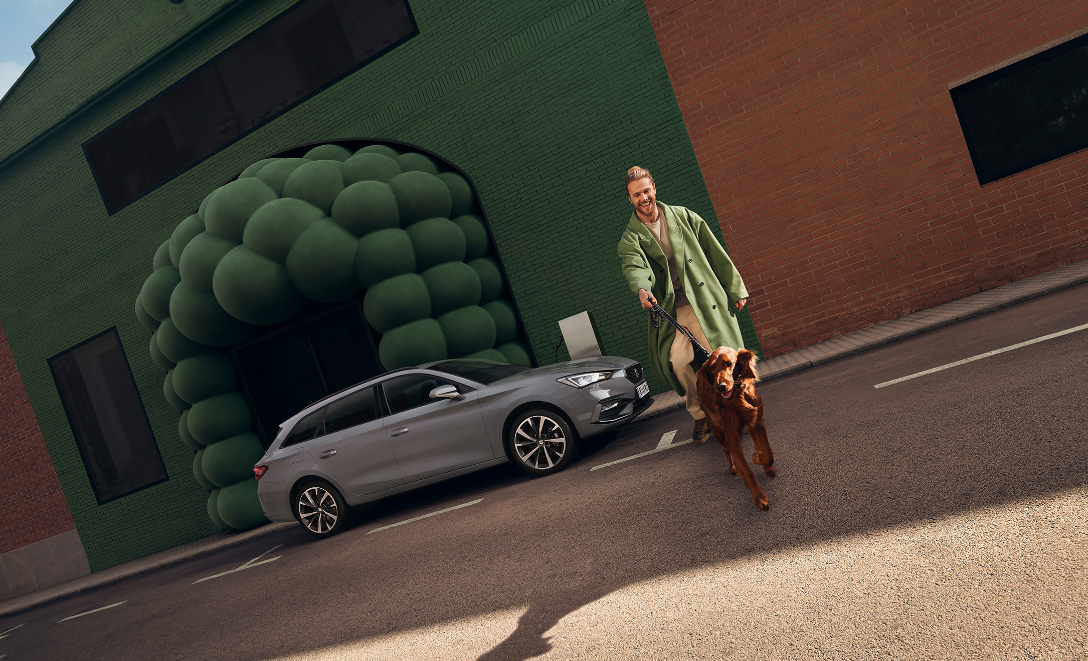 A man walking a dog toward the camera in front of a SEAT Leon Estate